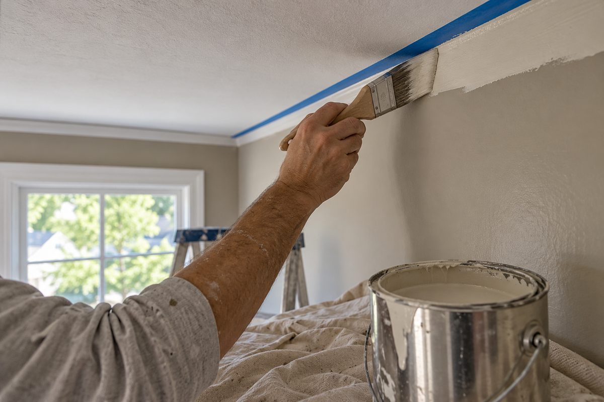 Precision sash brush cutting in clean ceiling line on freshly primed drywall.